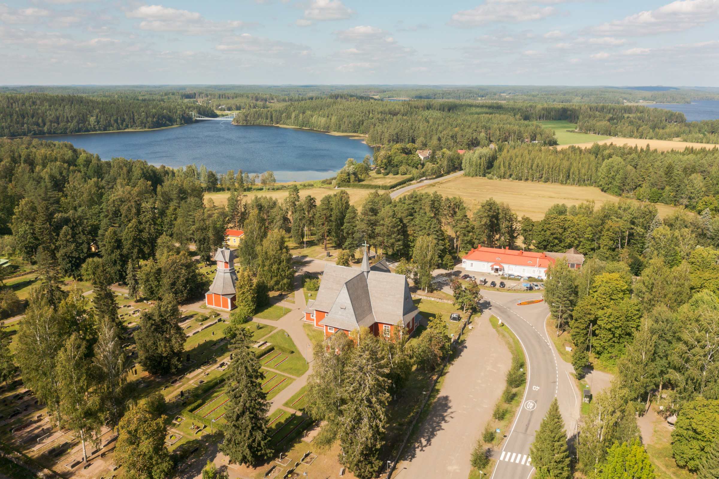 Iitin kirkonkylä ilmasta kuvattuna aurinkoisena elokuun päivänä. Kuvan keskellä vanha punainen kirkko ja ympärillä puita ja hautausmaata.